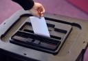 A person places a ballot paper into a ballot box.