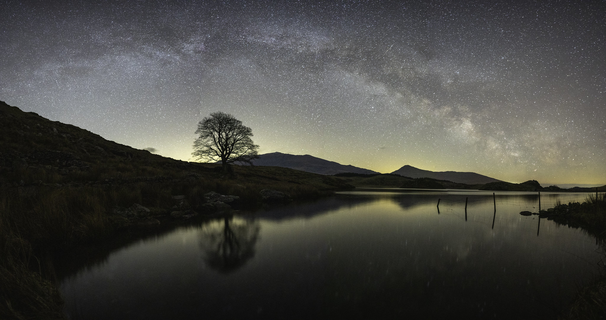 Panorama of Llyn y Dywarchen in Eryri. We planned this shot using an online app which detailed where the Milky Way was going to arch and what time. A few minutes before this image was taken the sky was cloudy and it was snowing. The sky cleared for