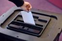 A person places a ballot paper into a ballot box.