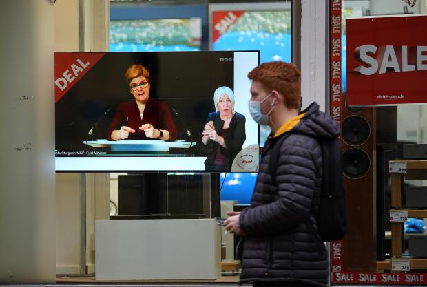 The Leader: Passers-by look at a tv screen in a Glasgow shop showing First Minister Nicola Sturgeon making a Covid-19 statement during a virtual sitting of the Scottish Parliament. Photo taken on December 29, 2021, via PA.