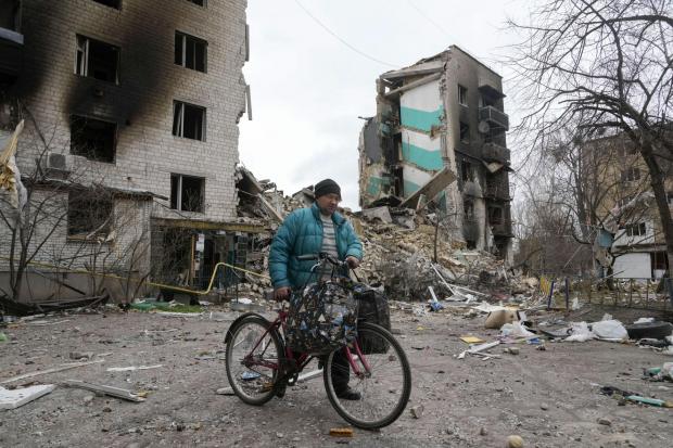 A man carries his belongings on a bike as he leaves his house, background, ruined in the Russian shelling in Borodyanka, Ukraine, Wednesday, April 6, 2022. (AP Photo/Efrem Lukatsky).