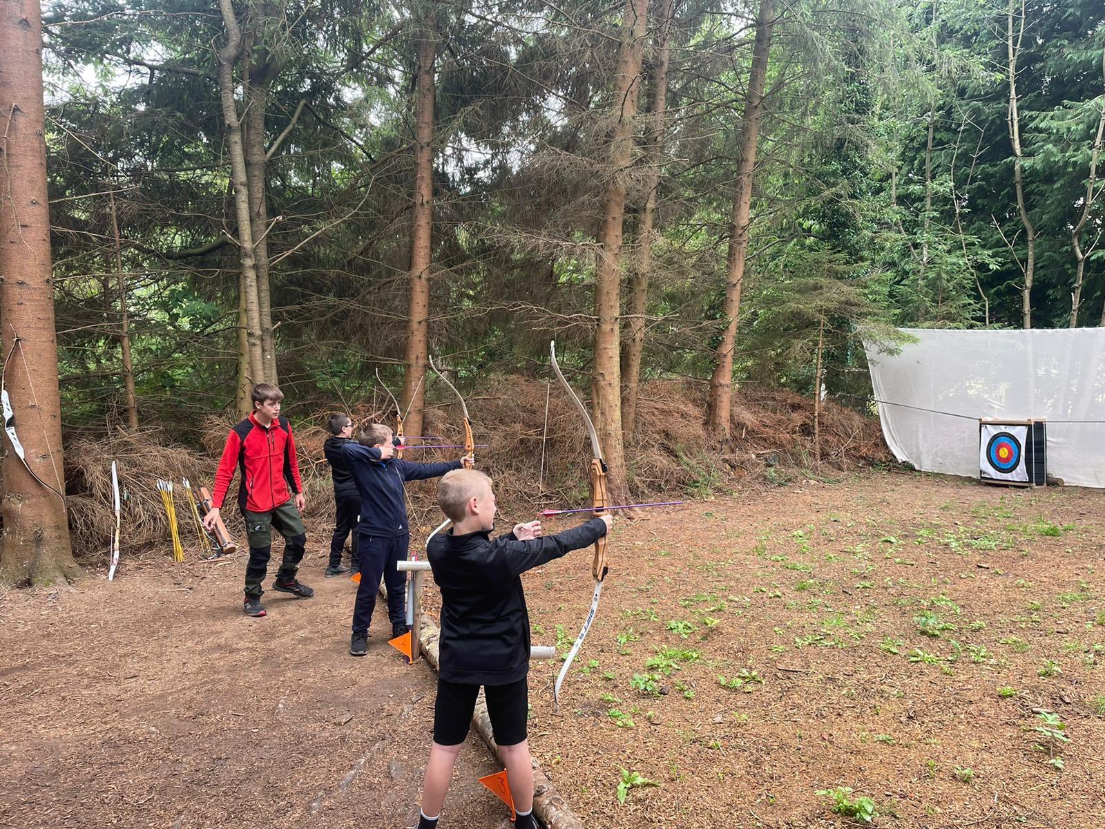 Three students get ready to have a go at archery under the watchful eye of the instructor.