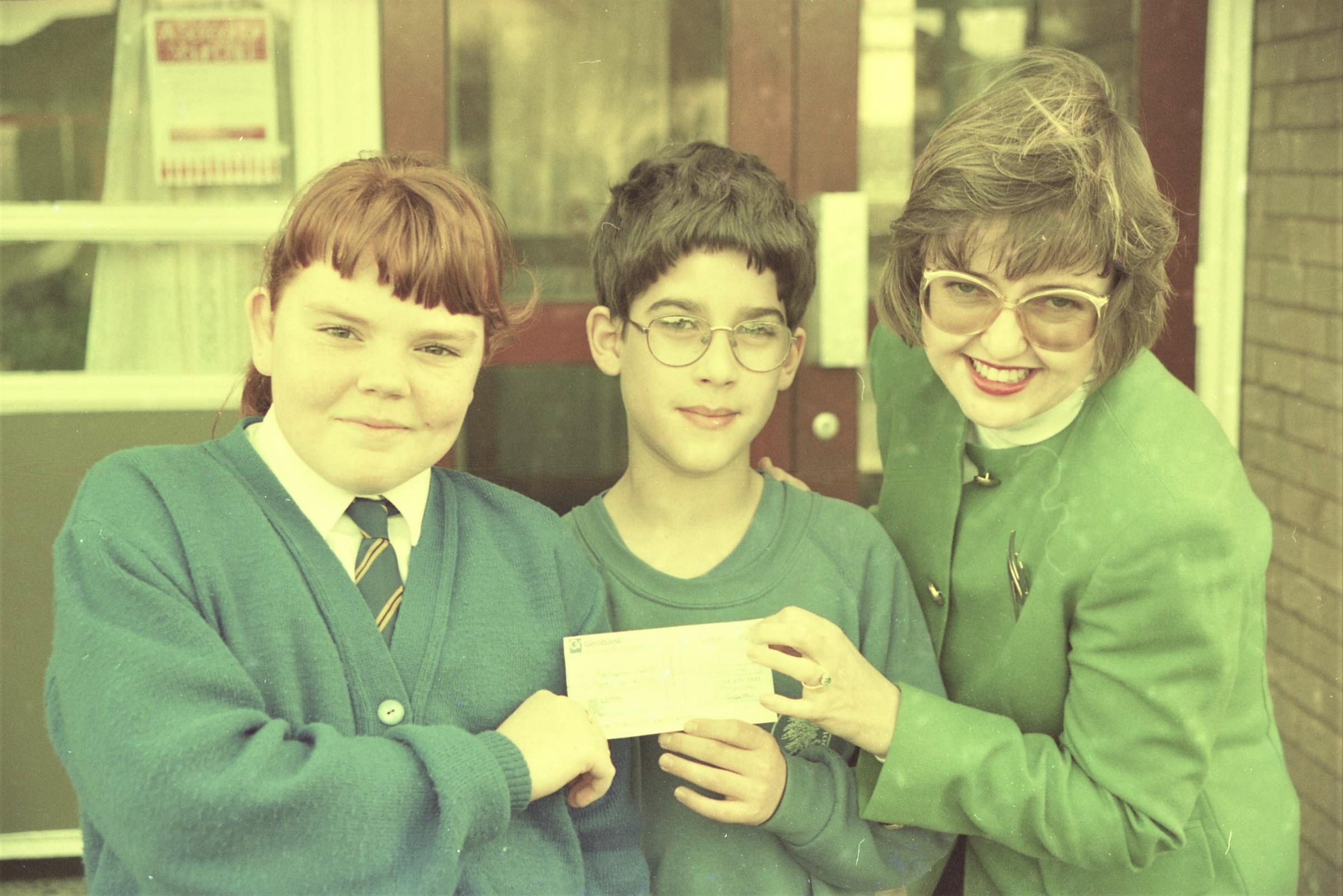 A cheque for proceeds from the Drury Primary School nativity is handed to Nightingale House Hospice appeals officer Julie Hinchliffe, by pupils Kelly Hughes and Ben Sheen, January 1994.