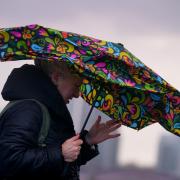 A woman struggles with an umbrella as she walks over Westminster Bridge during high winds and wet weather. Image PA.