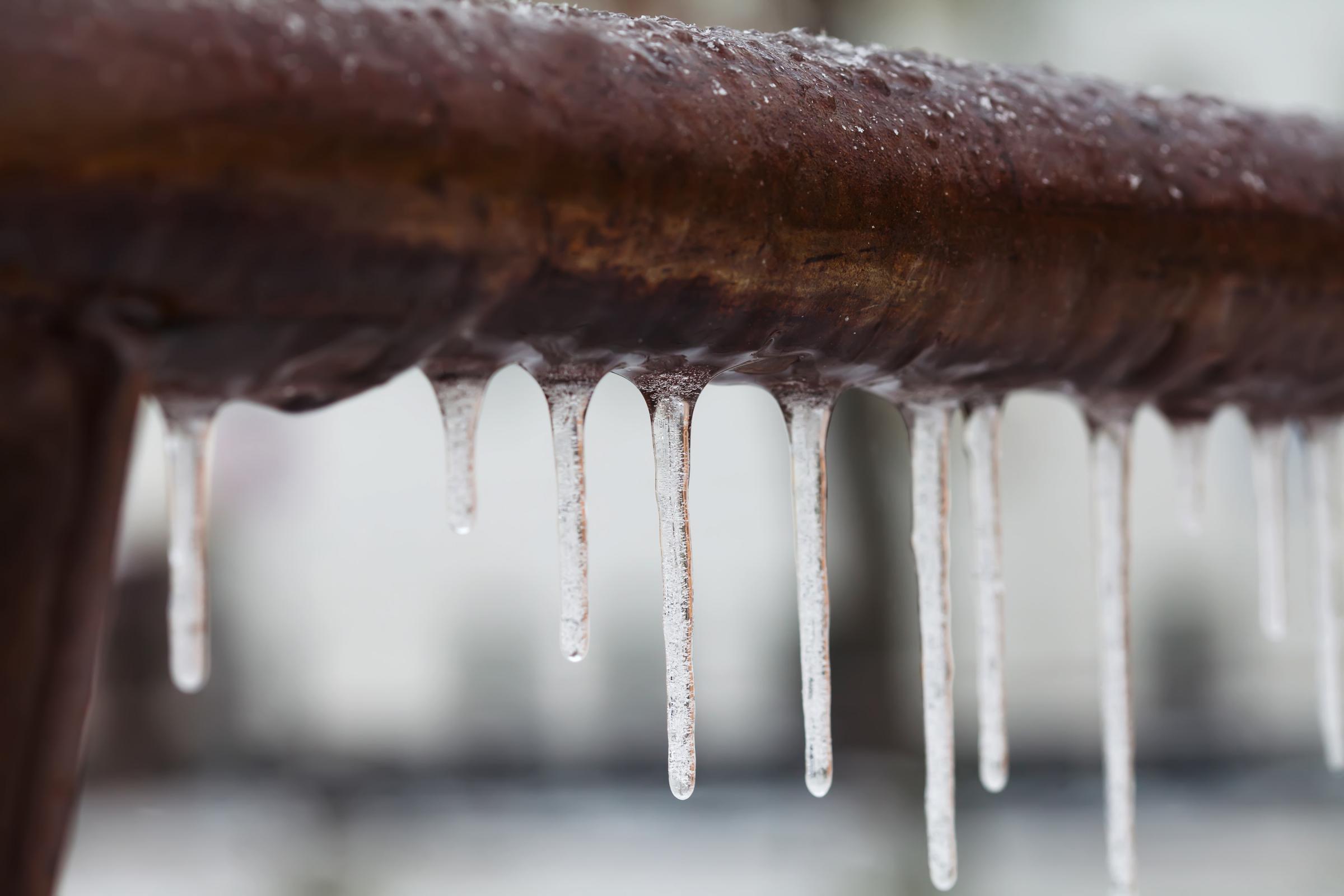 Icicles hanging from a brown pipe. 